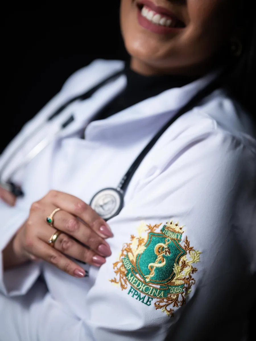 Detalhe do jaleco da Dra. Lara Costa com o brasão da faculdade de medicina